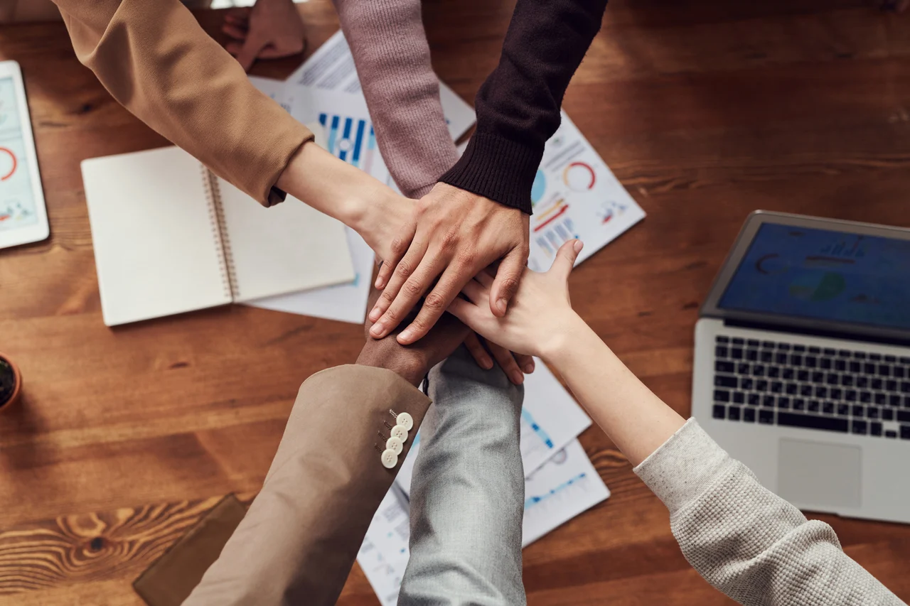 A team putting their hands together over a wooden desk.