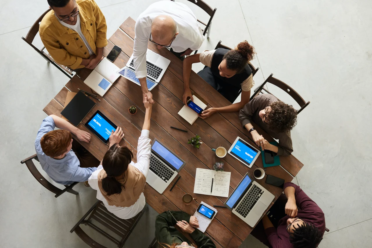 A group of colleagues all working together around a large wooden table.