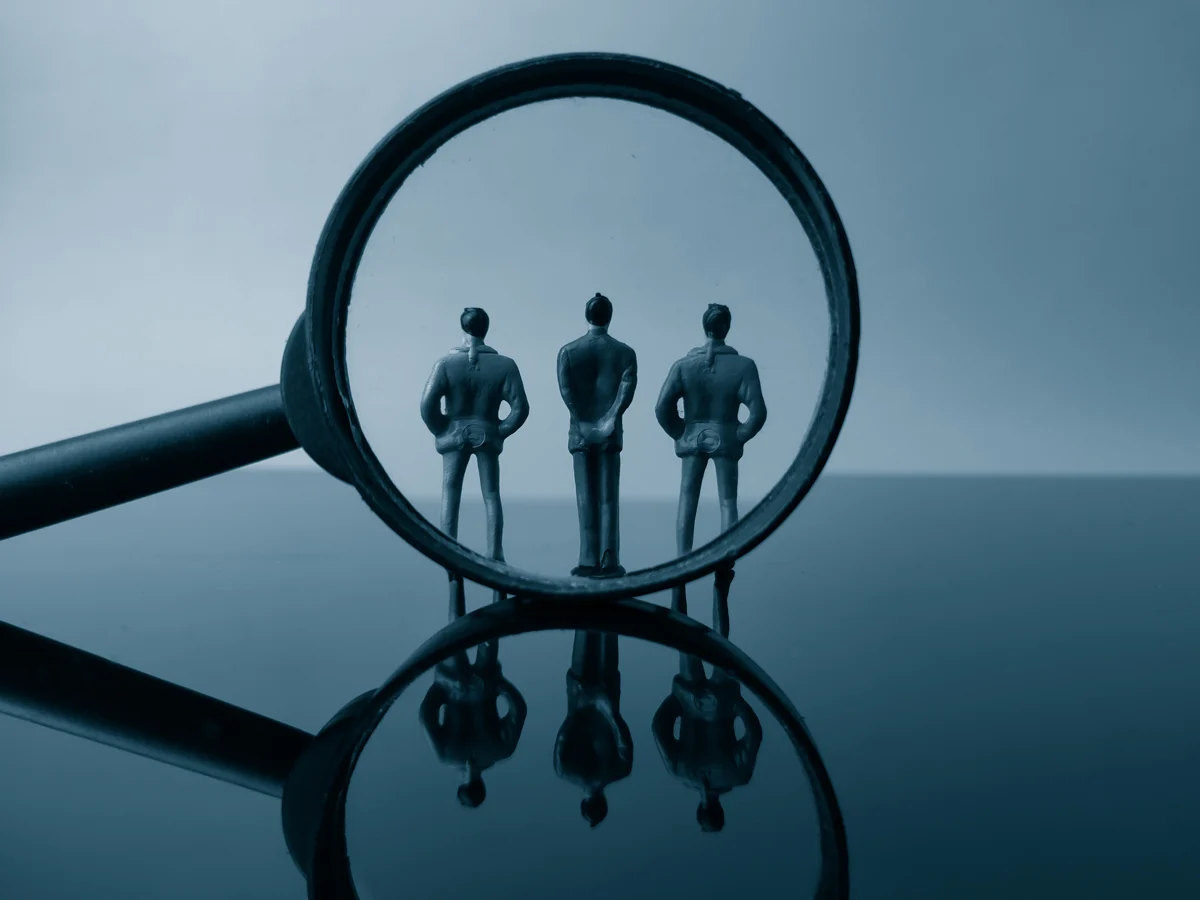 Three men in suits inside a magnifying glass.