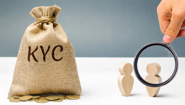 A sack with the letters 'KYC' on it next to a hand holding a magnifying glass.