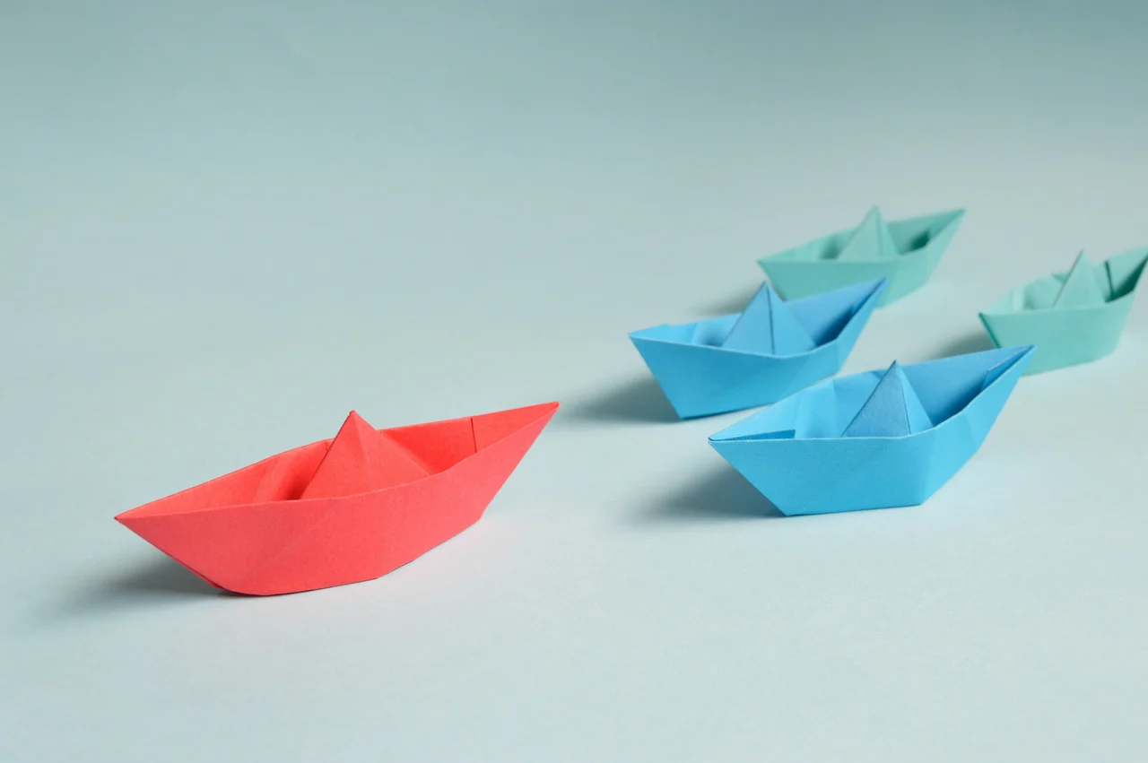 A red paper boat leading smaller blue and green ones.